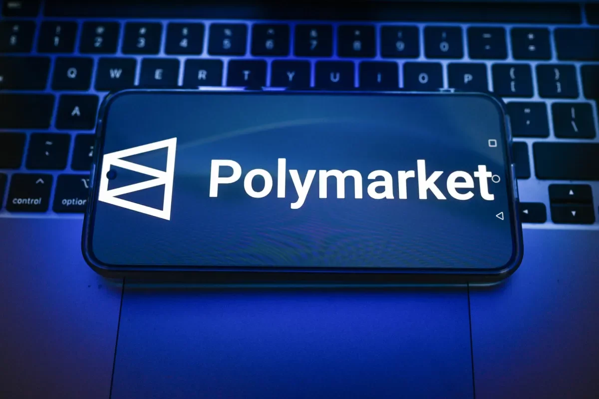 Logo de Polymarket en la pantalla de un móvil sobre un teclado iluminado en azul