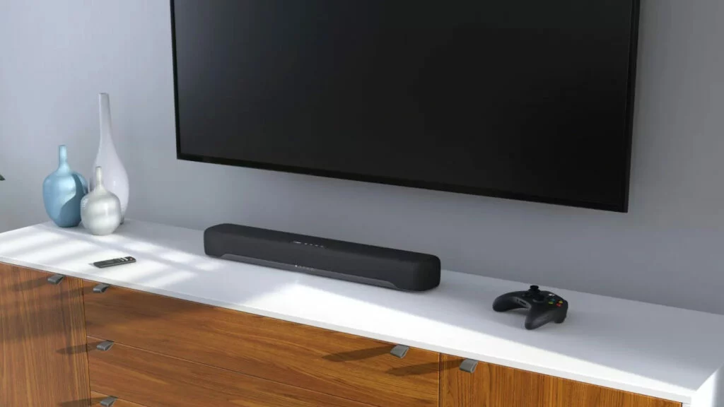 Barra de sonido Yamaha negra sobre mueble blanco bajo televisor con mando a distancia Barra de sonido Yamaha negra sobre mueble blanco bajo televisor con mando a distancia